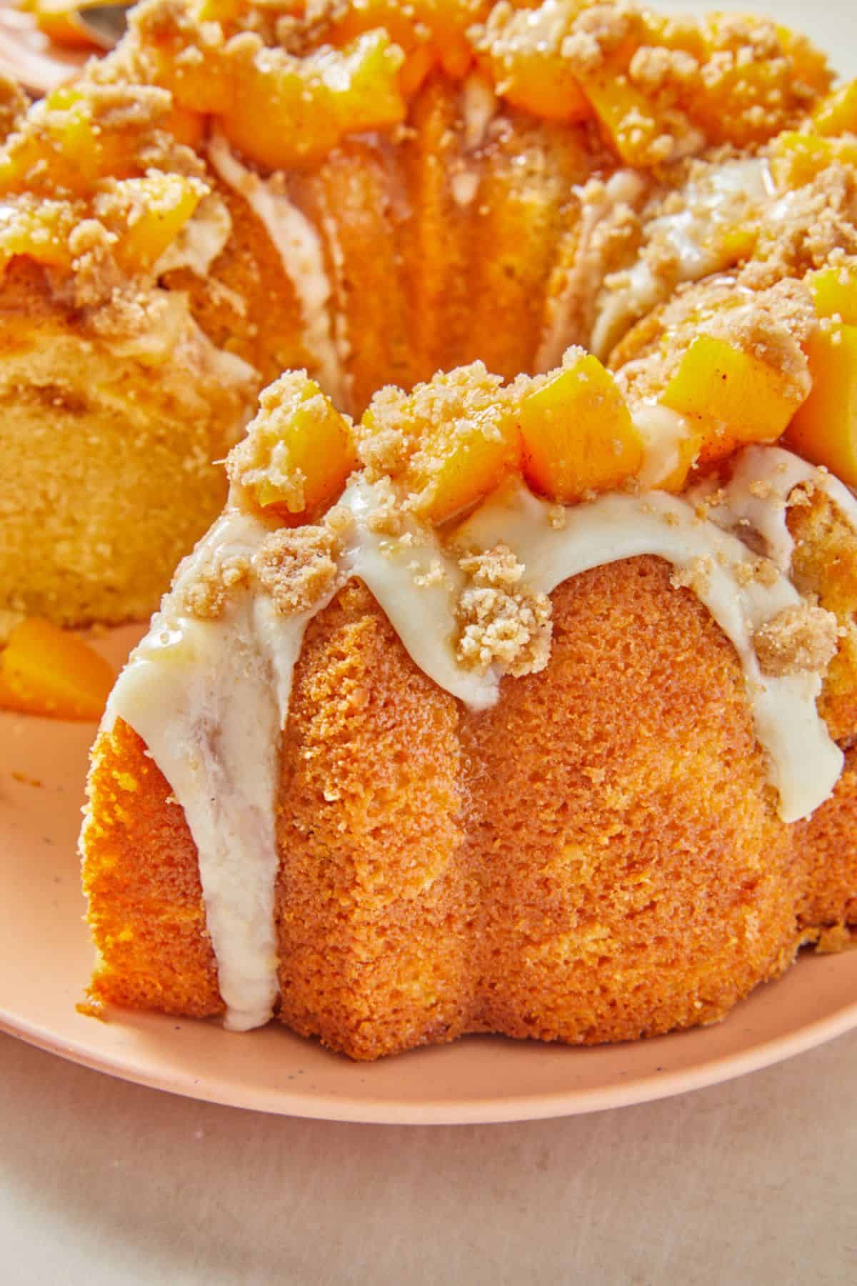 Closeup of a peach cobbler pound cake showing the rich texture of the cake with a topping of diced peaches, crumbles, and drizzled icing on a pink plate