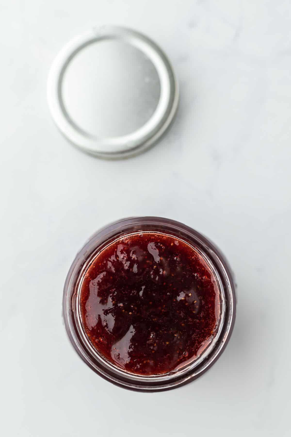 Overhead shot of strawberry preserves on a glass jar with the lid next to it