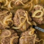 Overhead shot of a skillet full of hamburger steaks covered in a thick onion gravy with a spoon in it