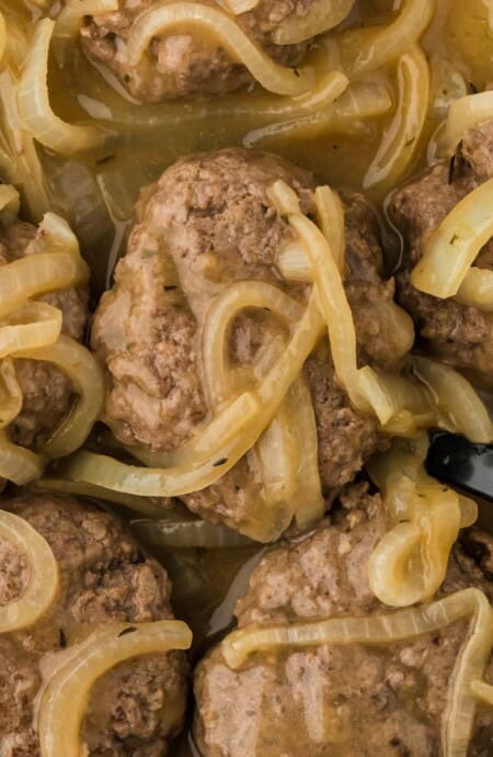 Overhead shot of a skillet full of hamburger steaks covered in a thick onion gravy with a spoon in it