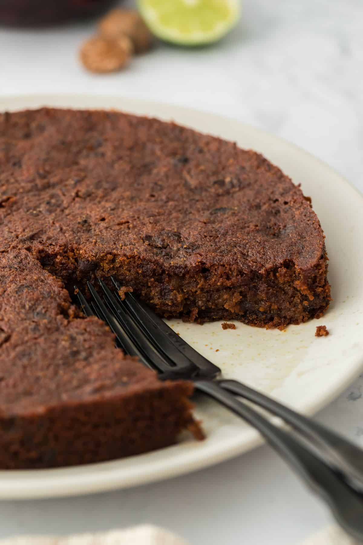 A Jamaican black cake with a slice missing in a white place, with black forks resting where the slice should be

