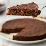 A slice of black cake being lifted from whole cake on white background