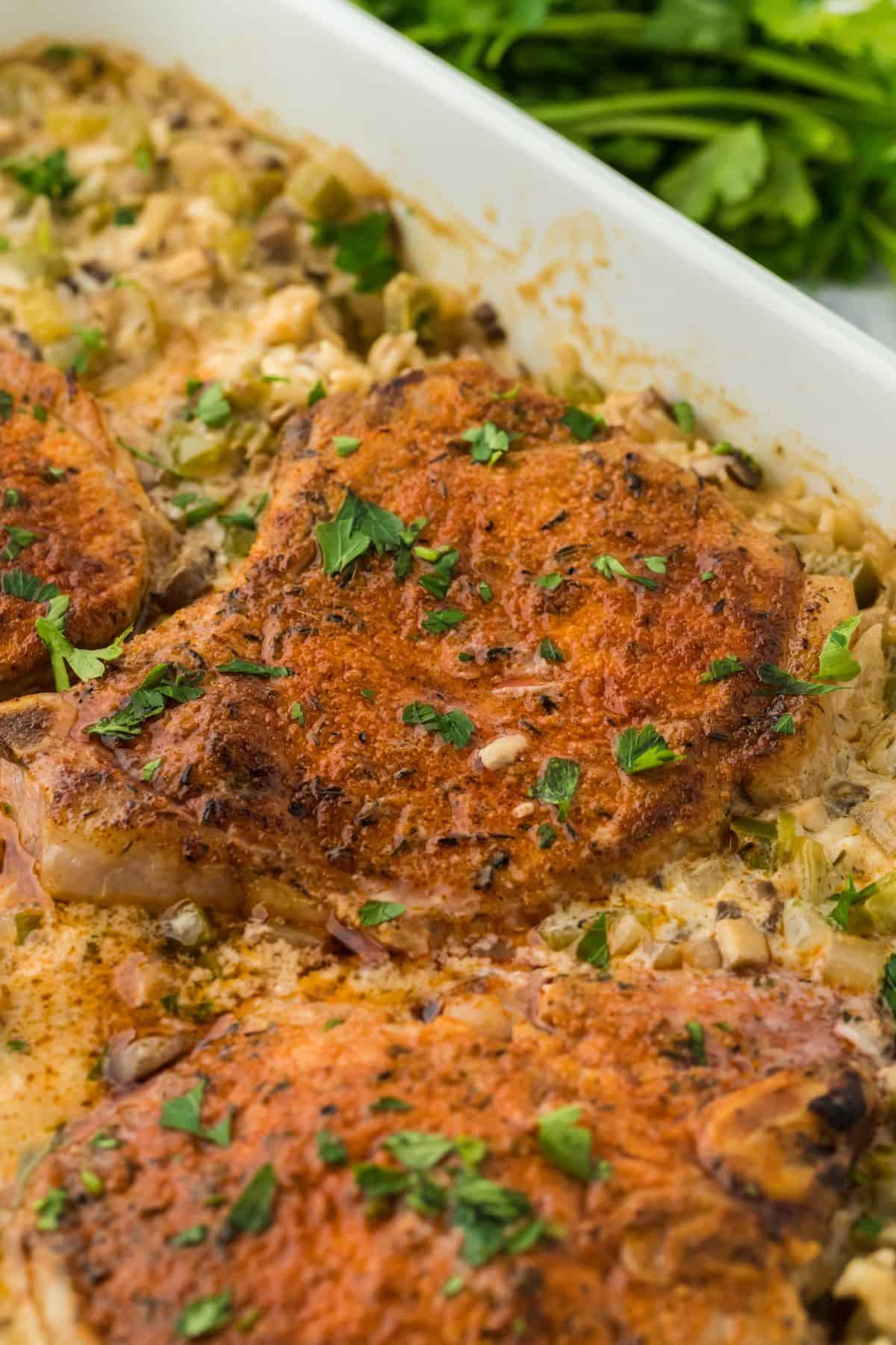 Closeup of pork chops of the pork chop casserole in a white rectangular baking dish, garnished with chopped parsley