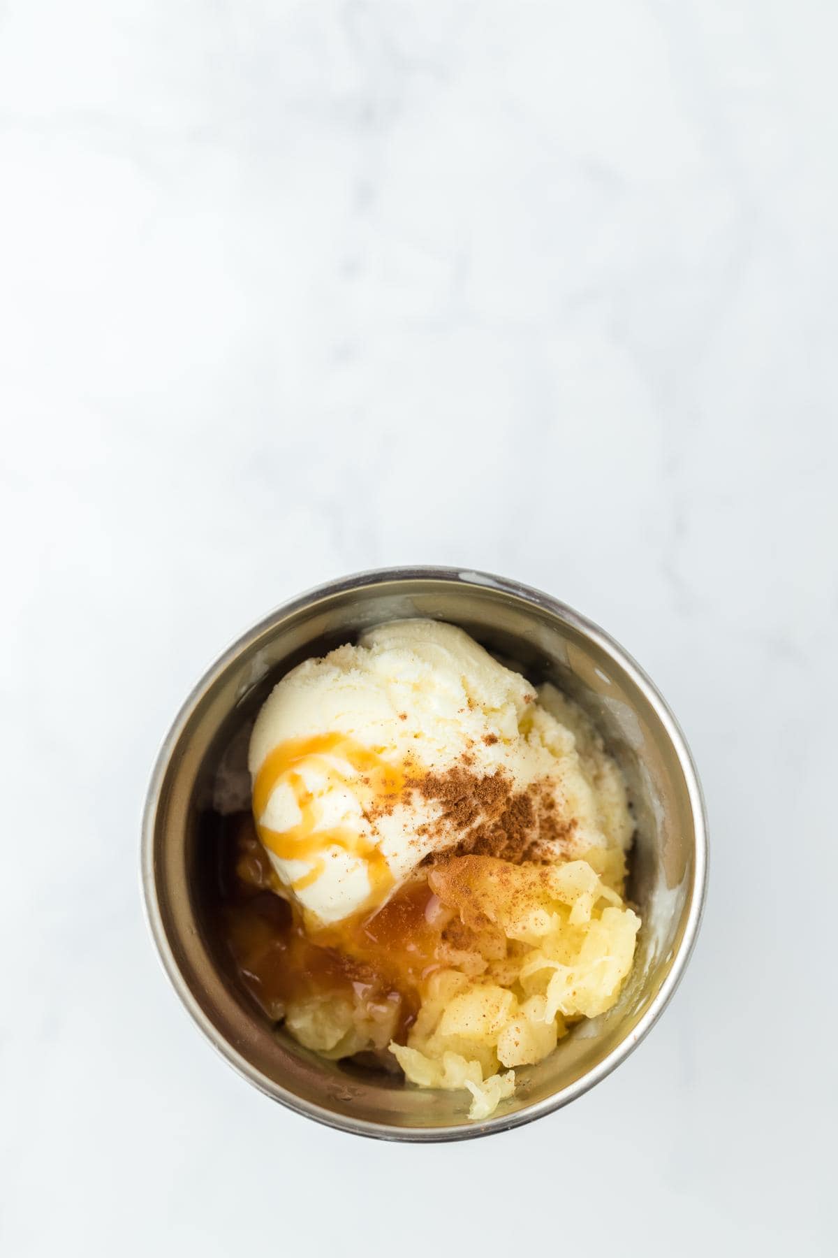 Ice cream, pineapple sherbet, crushed pineapple, caramel sauce, and cinnamon in a metal milkshake cup