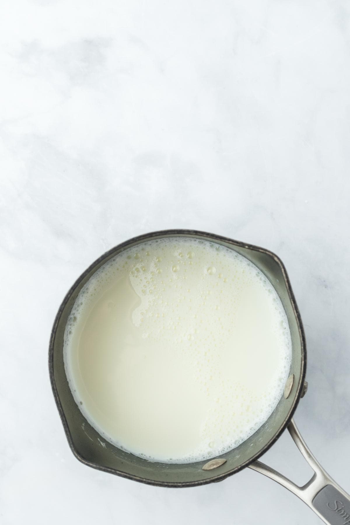 A metal saucepan on a white surface with heated milk