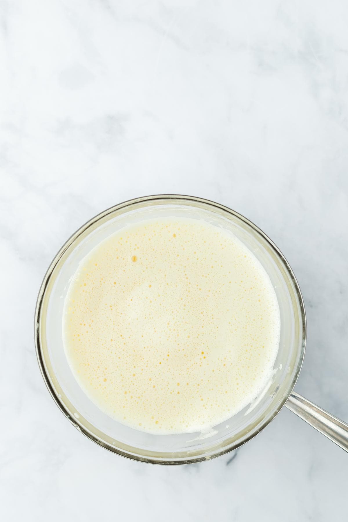 A clear glass bowl holds a pale yellow, bubbling custard, showing it's been heated