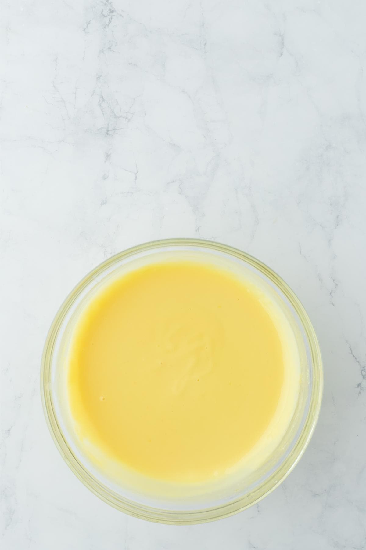 A clear glass bowl contains a smooth, pale yellow, thickened custard