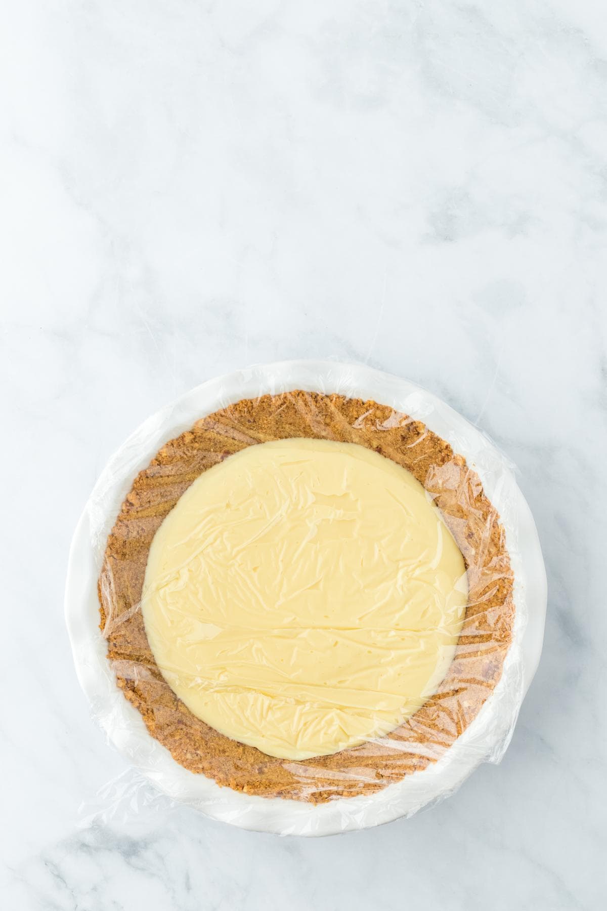 Prepared tart crust filled with chilled custard, covered in plastic wrap, ready to be refrigerated