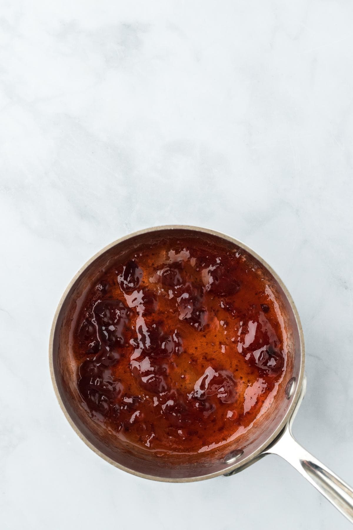 Strawberry preserves simmering in a saucepan, thick and glossy, ready to top the strawberry custard pie