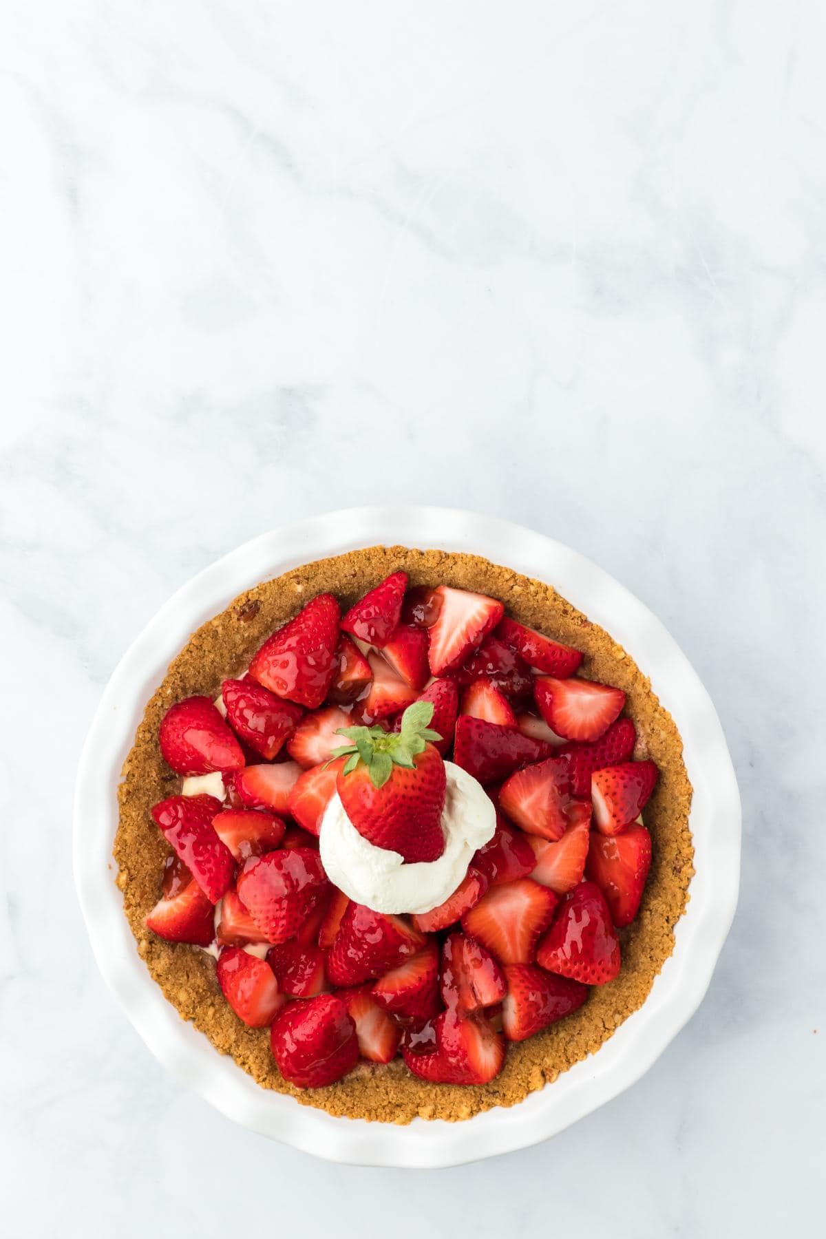 Finished strawberry custard pie topped with fresh glazed strawberries and a dollop of whipped cream in the center