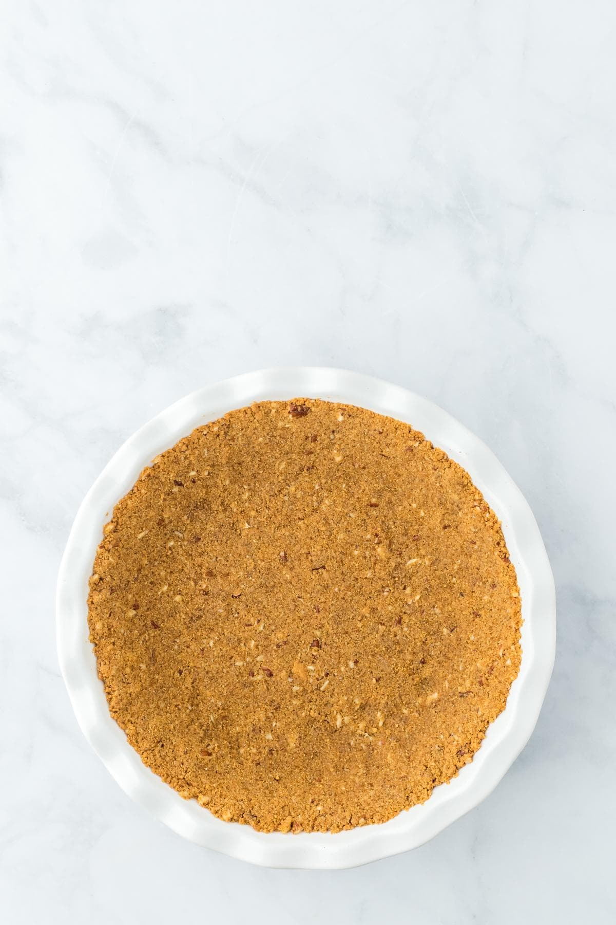 A golden-brown, baked pecan graham cracker crust resting inside a white fluted pie dish for strawberry custard pie