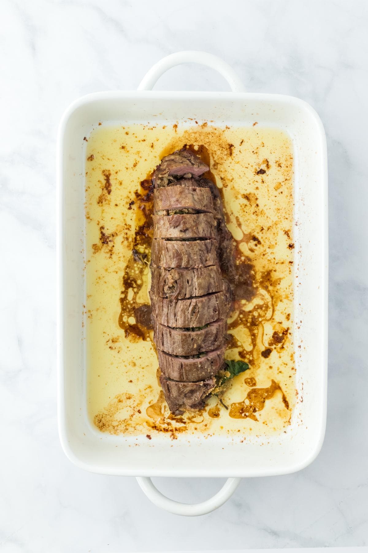 Cooked and sliced stuffed flank steak in a baking dish