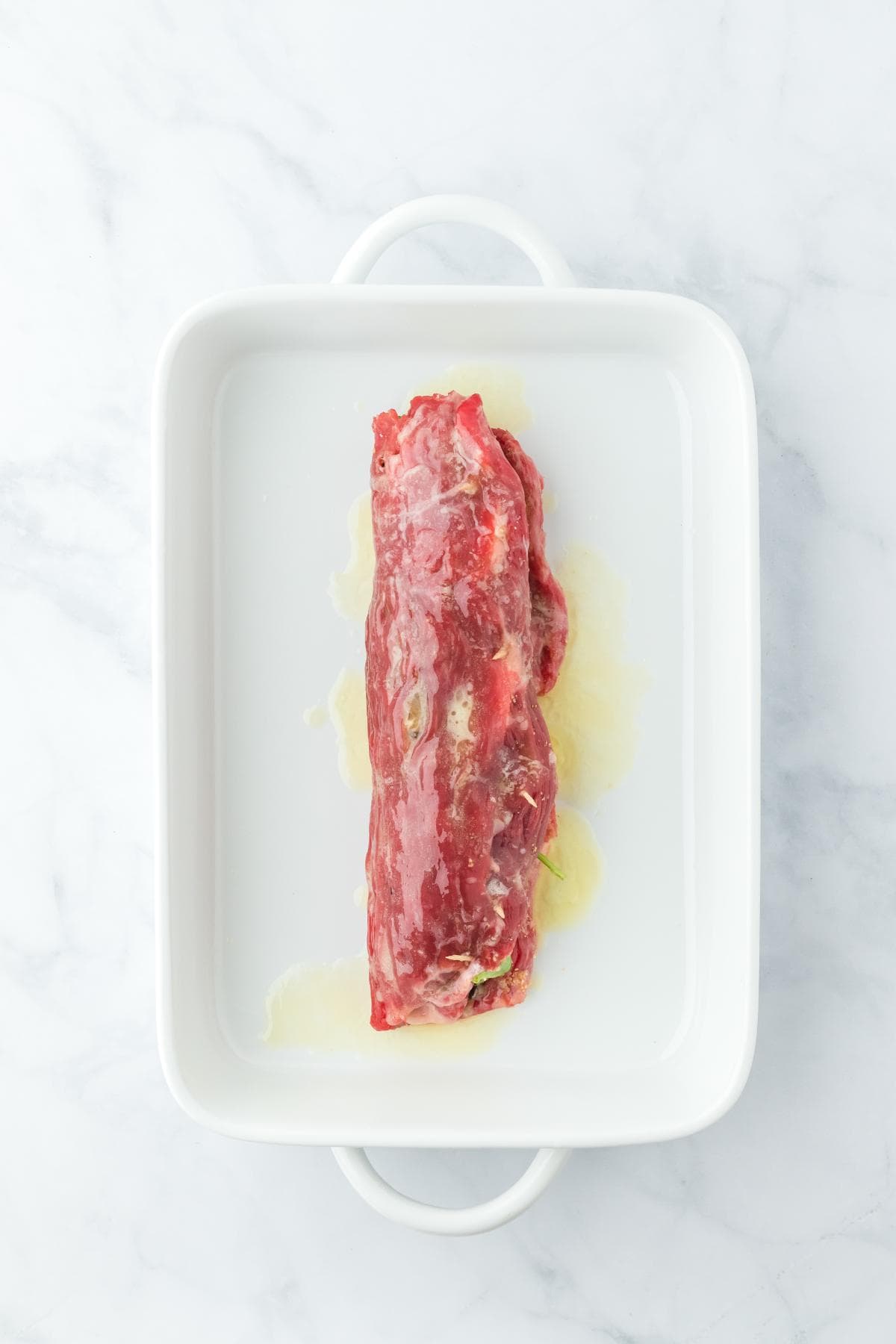 Rolled and stuffed flank steak placed in a white baking dish before cooking