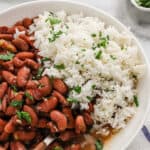A close up of red beans and rice on a white plate with a spoon digging in