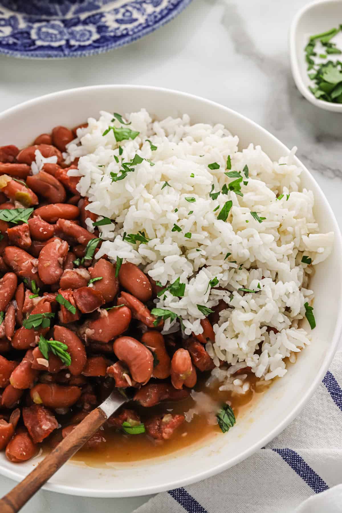 A close up of red beans and rice on a white plate with a spoon digging in
