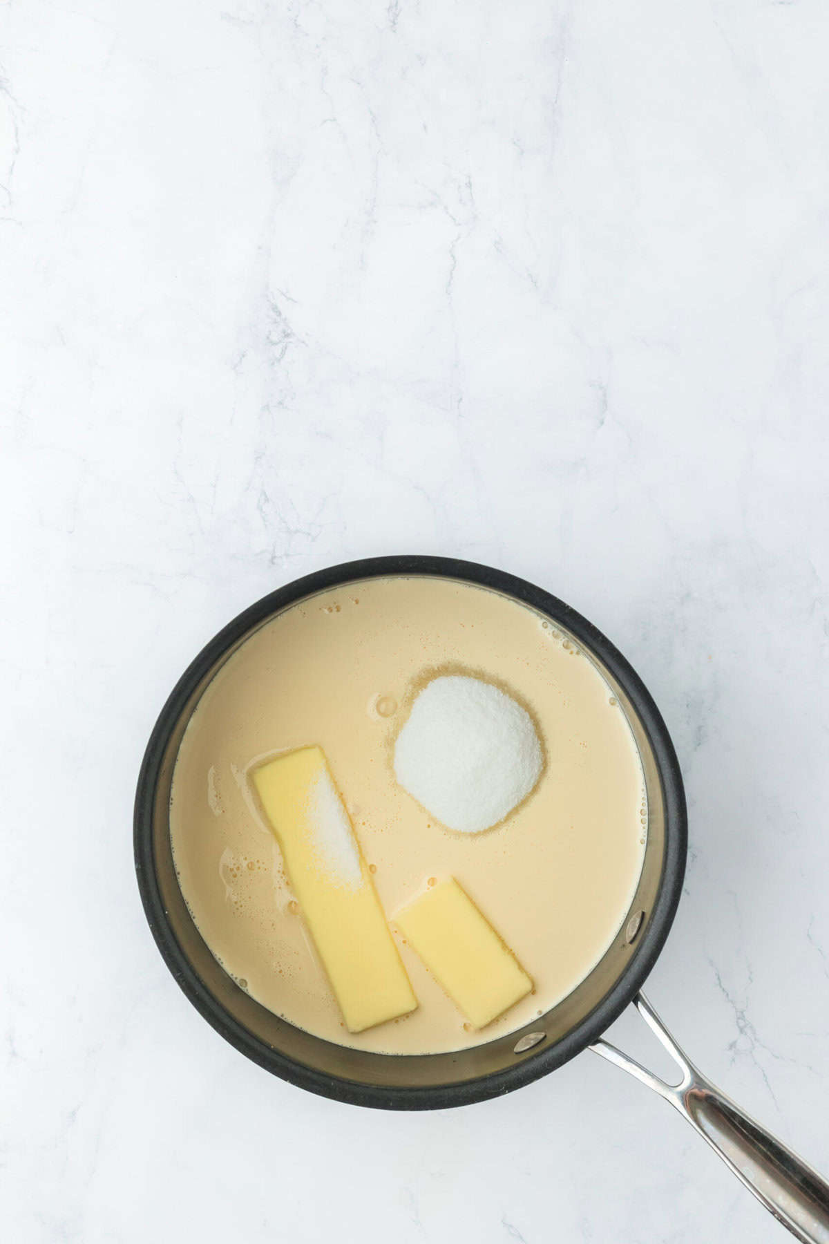 Butter, sugar, evaporated milk in a saucepan on white countertop melting together