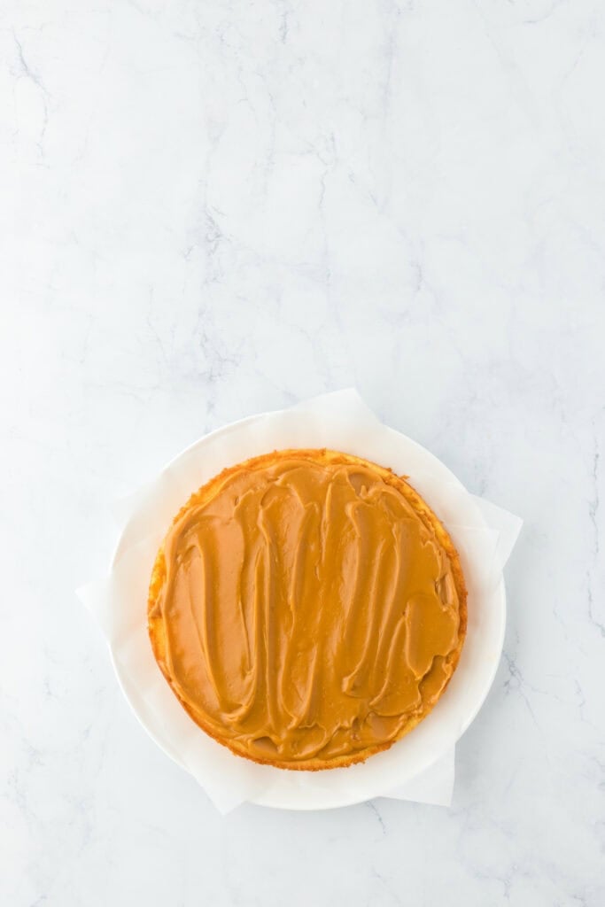 Caramel cake layers being iced and stacked on white countertop