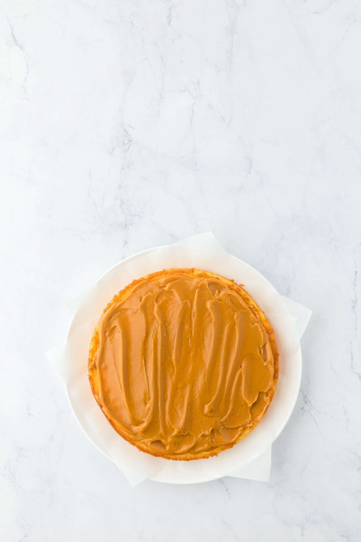 Caramel cake layers being iced and stacked on white countertop