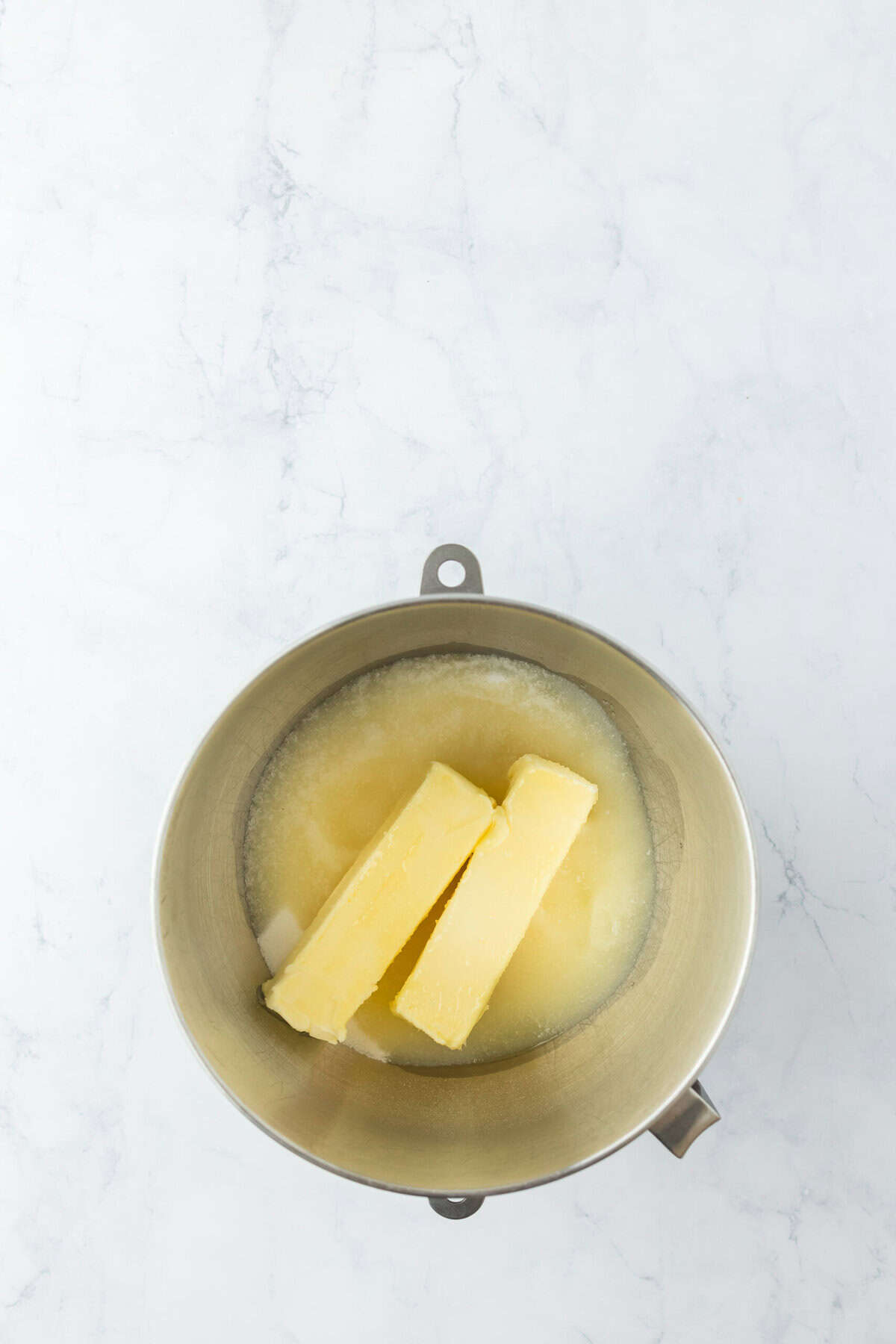 Butter, sugar and oil in a stand mixer mixing on white countertop