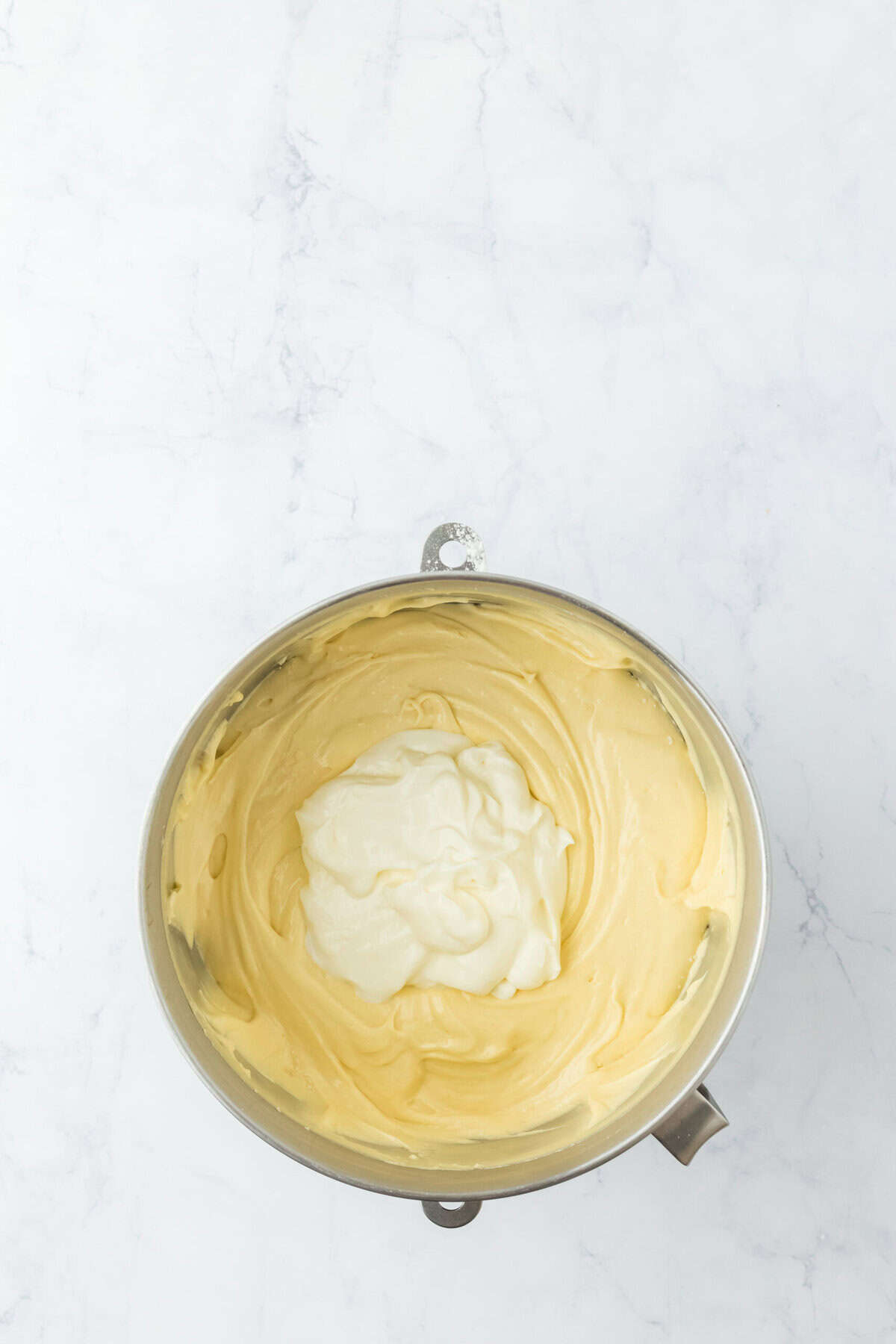 Sour cream being added to cake mix in stand mixer bowl on white countertop