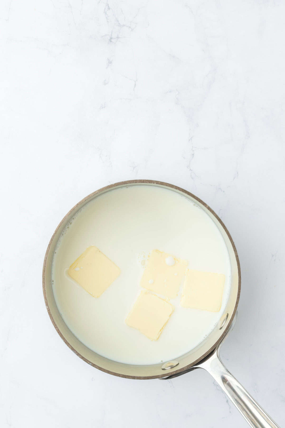 Coconut milk and butter in a saucepan melting together on white countertop