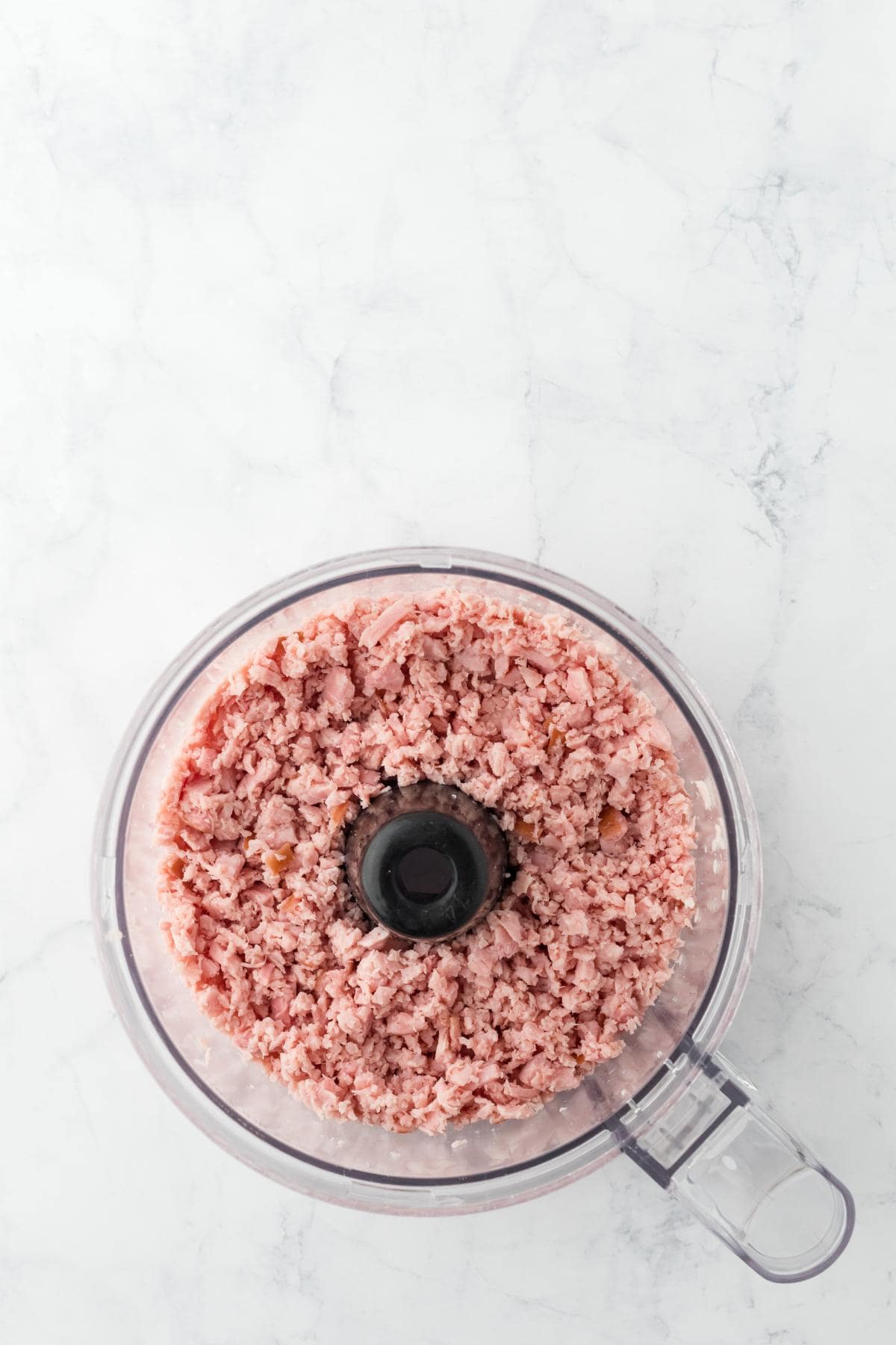 Finely chopped ham filling the bowl of a food processor after processing