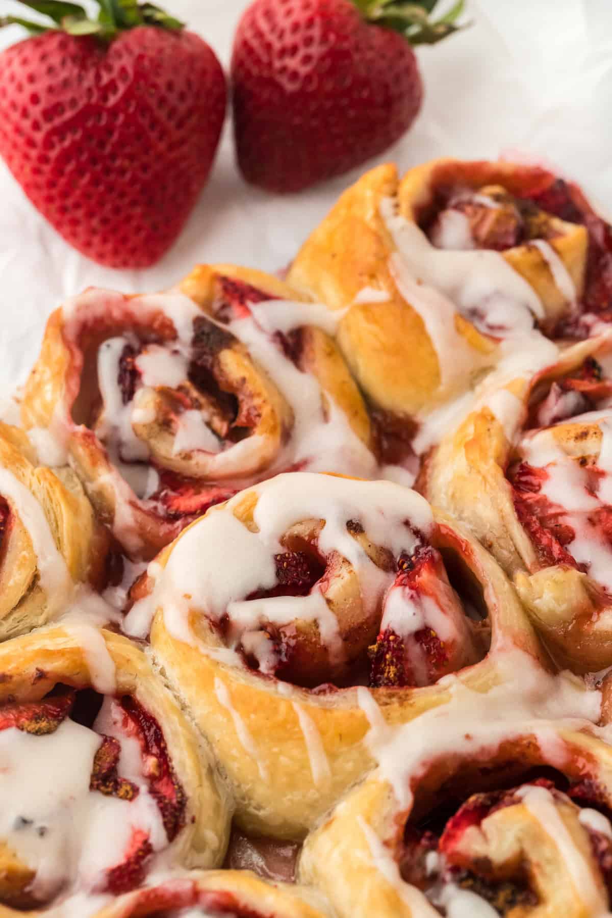 Easy strawberry cinnamon rolls drizzled with icing with two strawberries in the background