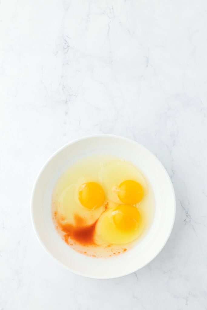 Eggs and hot sauce in a white bowl on countertop