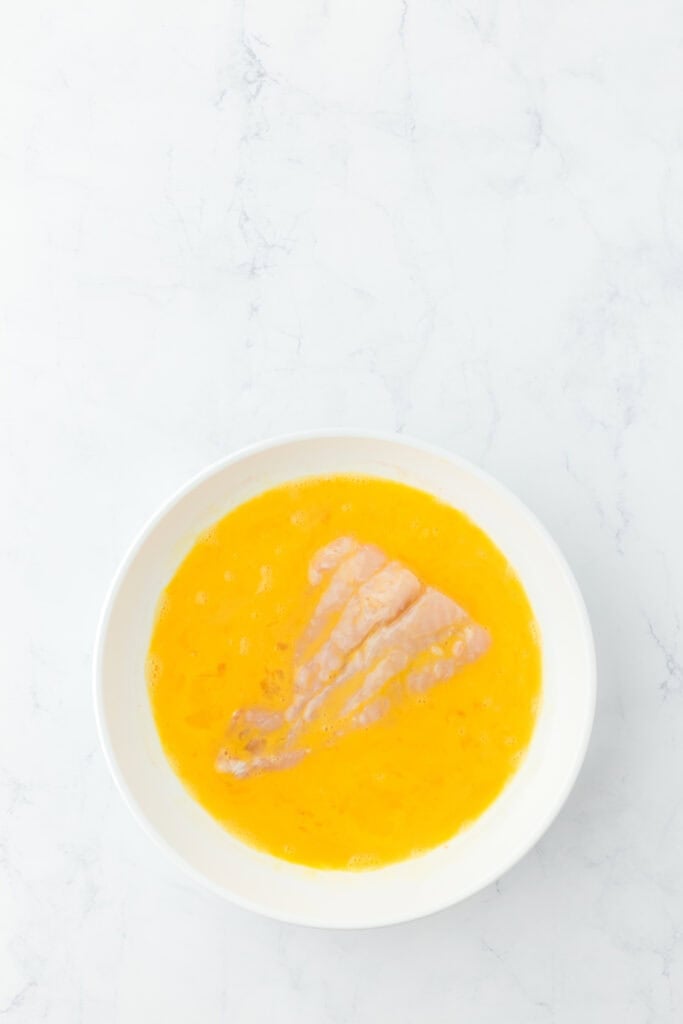 Catfish filet in egg batter in glass bowl