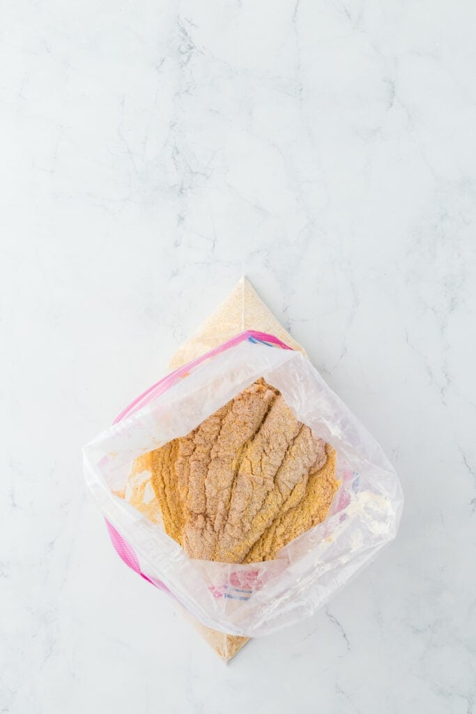 Catfish being dredged in cornmeal on countertop