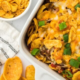 freshly baked frito pie in a casserole dish on a white background with fritos in the background