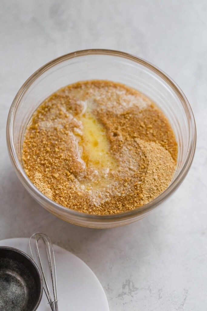 Butter added to graham cracker crumbs in a glass bowl