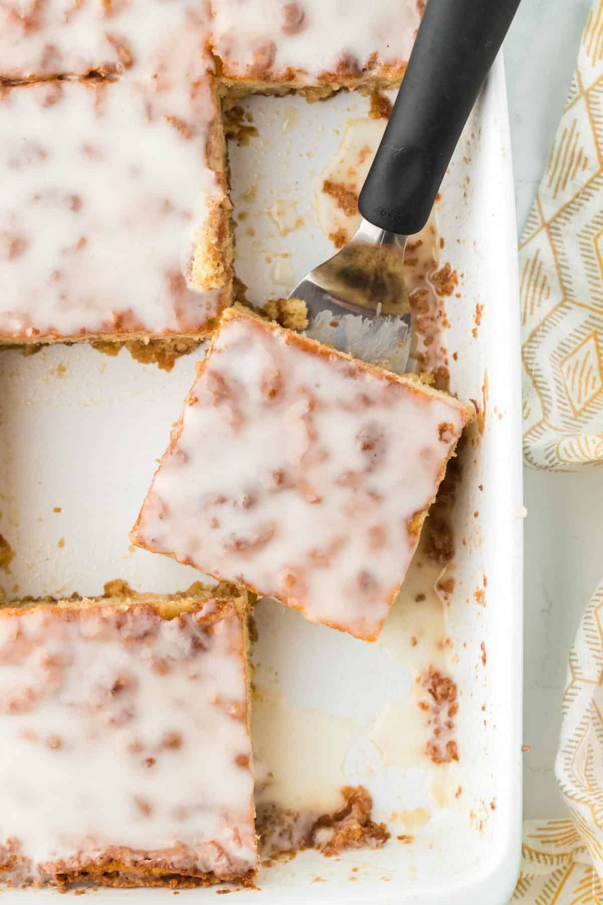 Honey bun cake slice lifted from pan with spatula, topped with glaze
