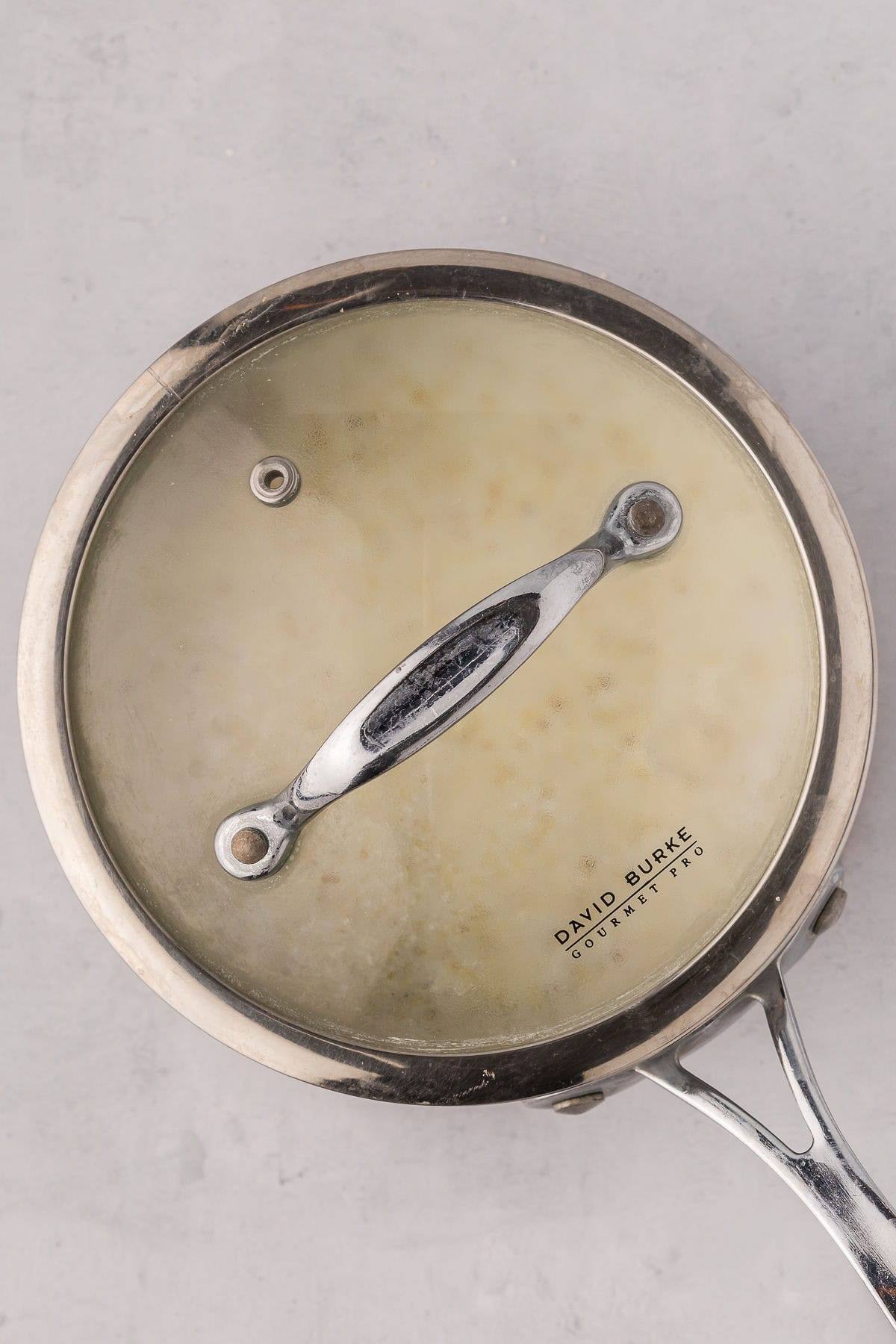 A saucepan covered with a glass lid as the grits simmer