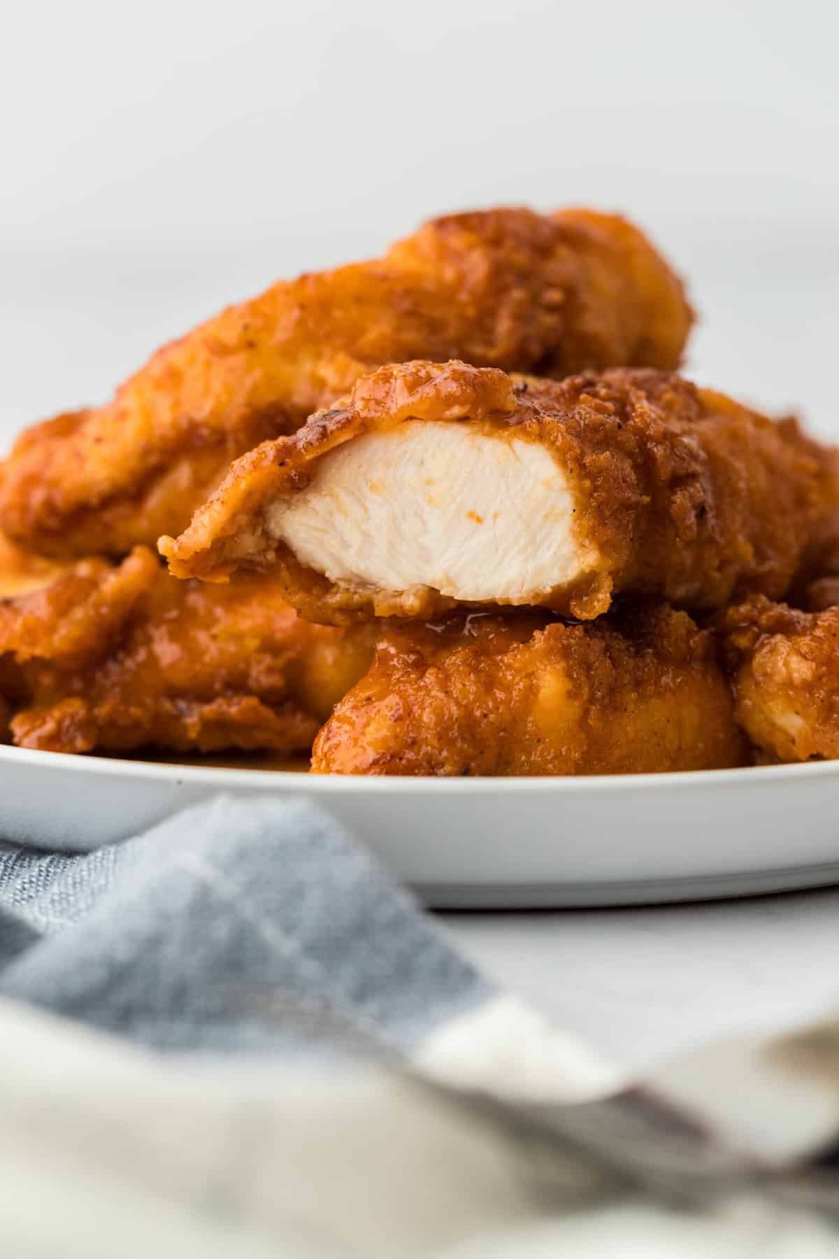 A white plate filled with hot honey chicken tenders with one cut open to see the inside juicy chicken