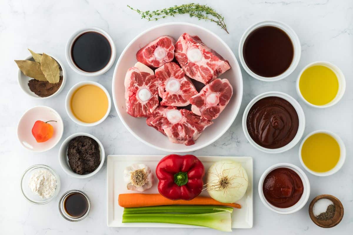 Overhead shot of ingredients to make Jamaican Oxtail on a white surface before cooking