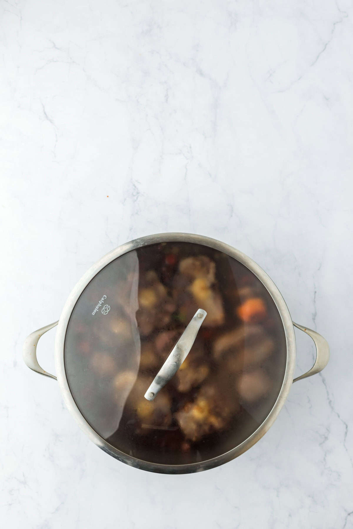 Covered pot with oxtail recipe cooking on white background