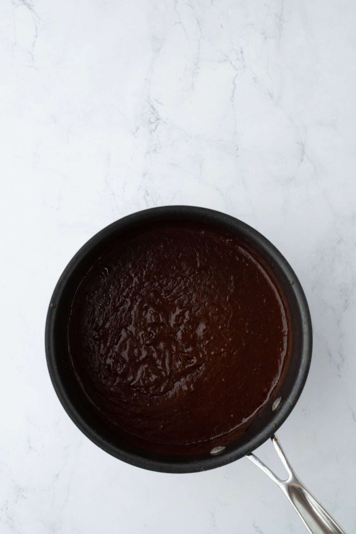 Bubbling jerk bbq sauce in a small pot cooking on white countertop