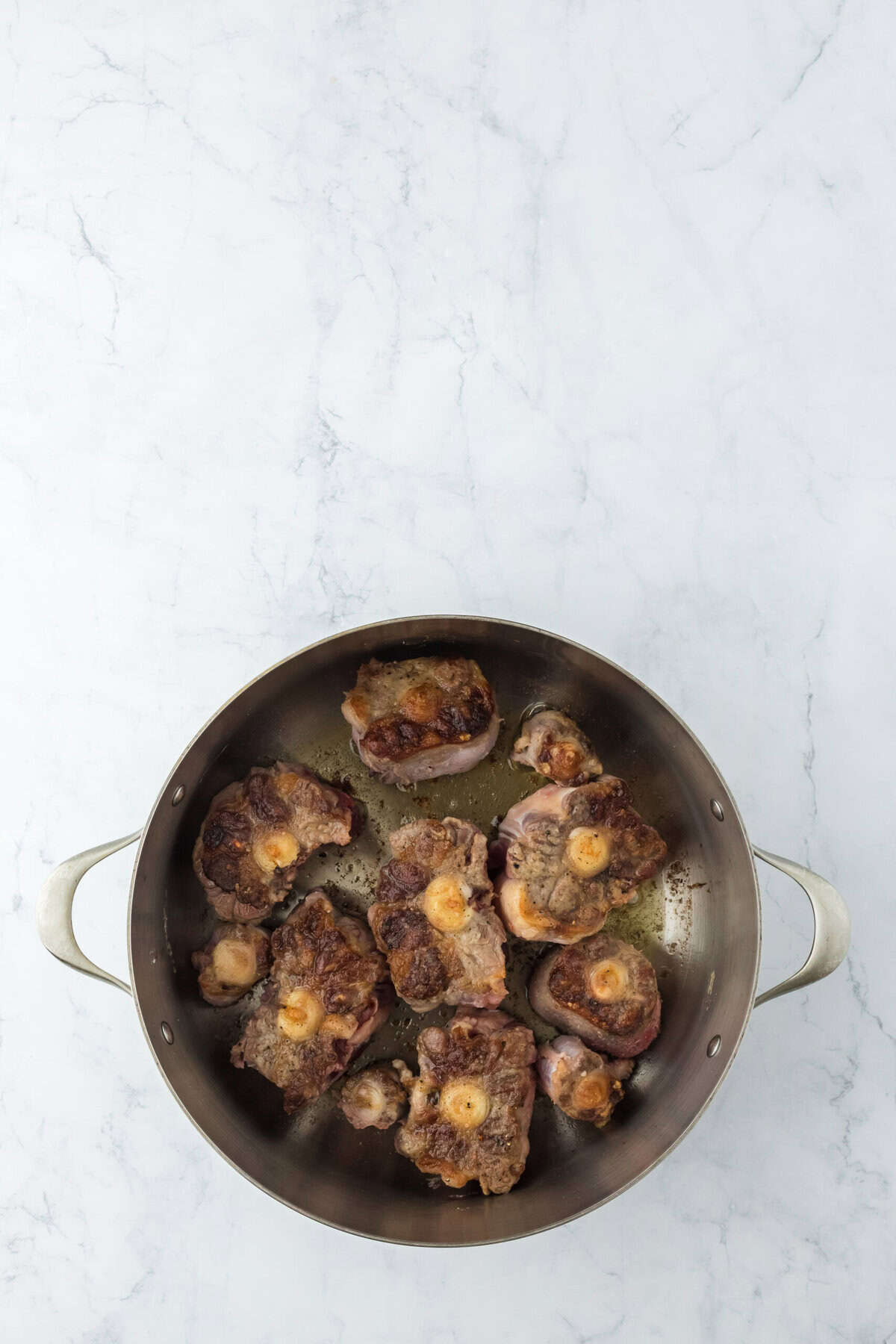 Oxtails cooking in a skillet in oil on white countertop