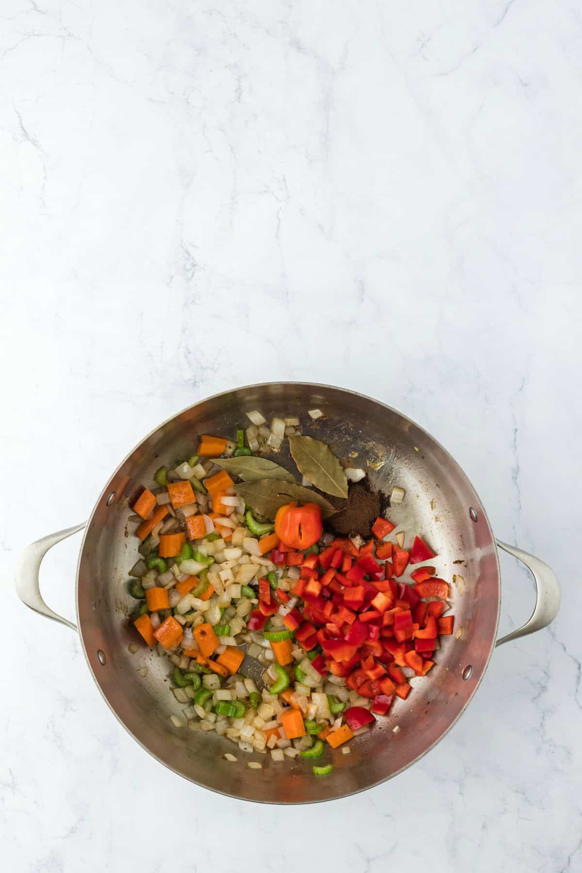 Habanero pepper along with bay leaves and veggies in pan cooking on white background