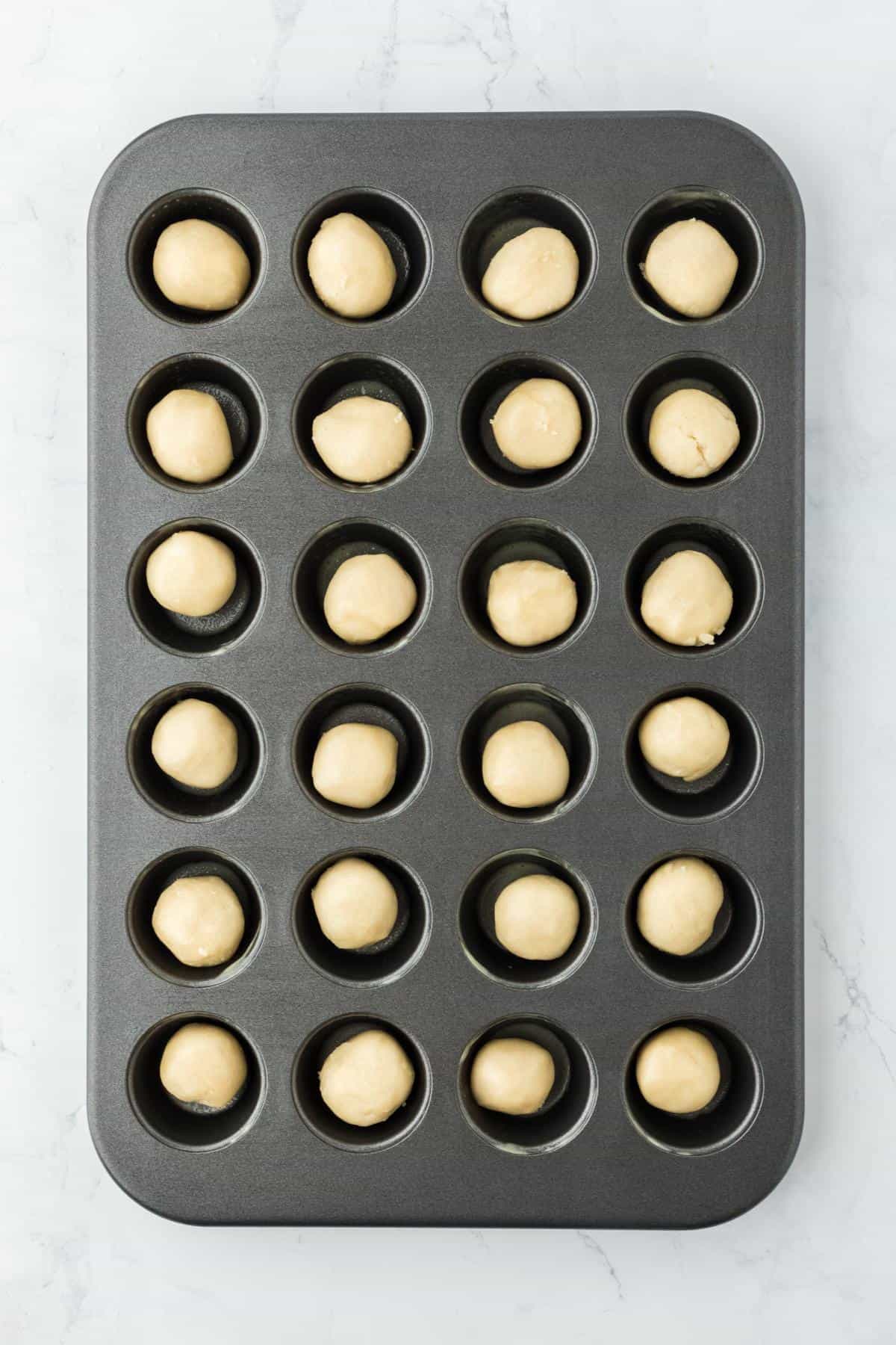 Balls of cookie dough arranged in a mini muffin tin before baking