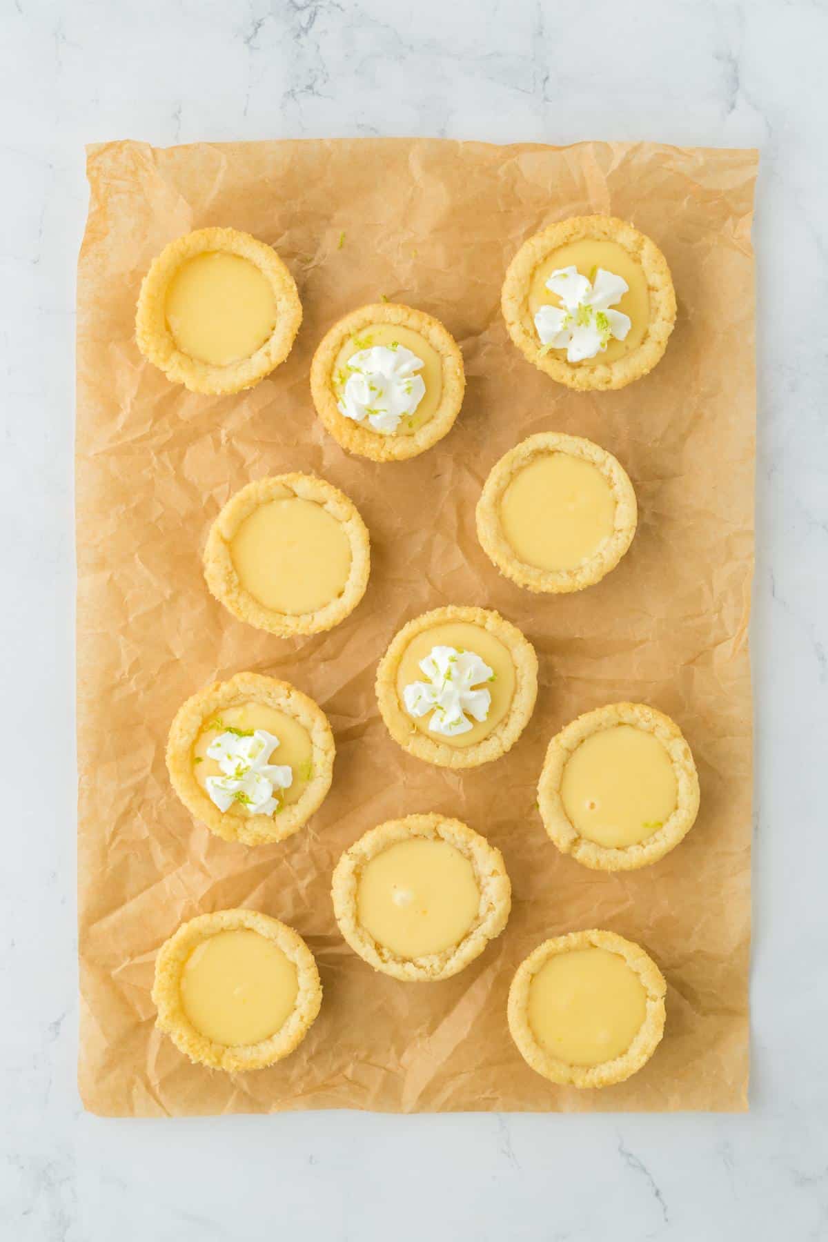 A group of filled key lime pie cookie cups on parchment paper, some topped with whipped cream