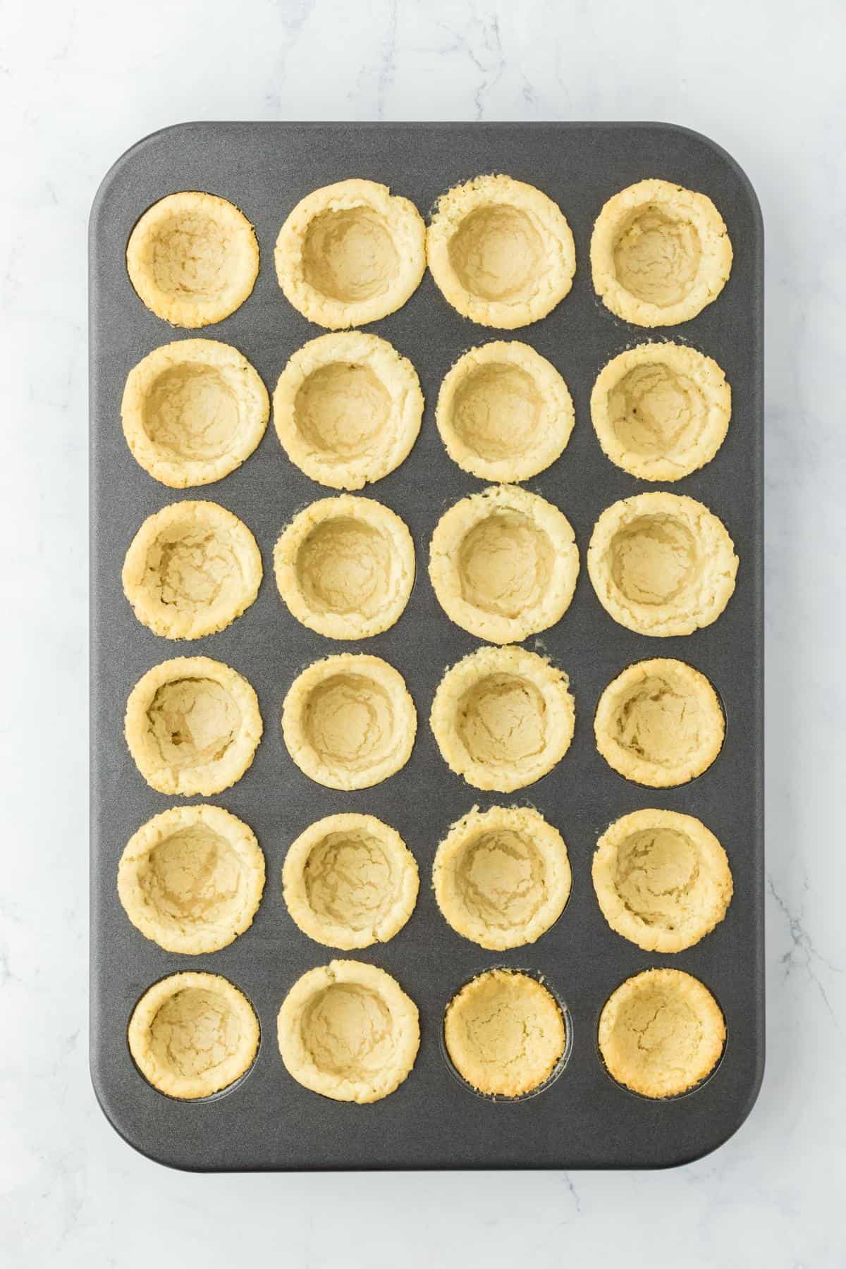 Cookie cups in the tin with centers pressed down to form wells
