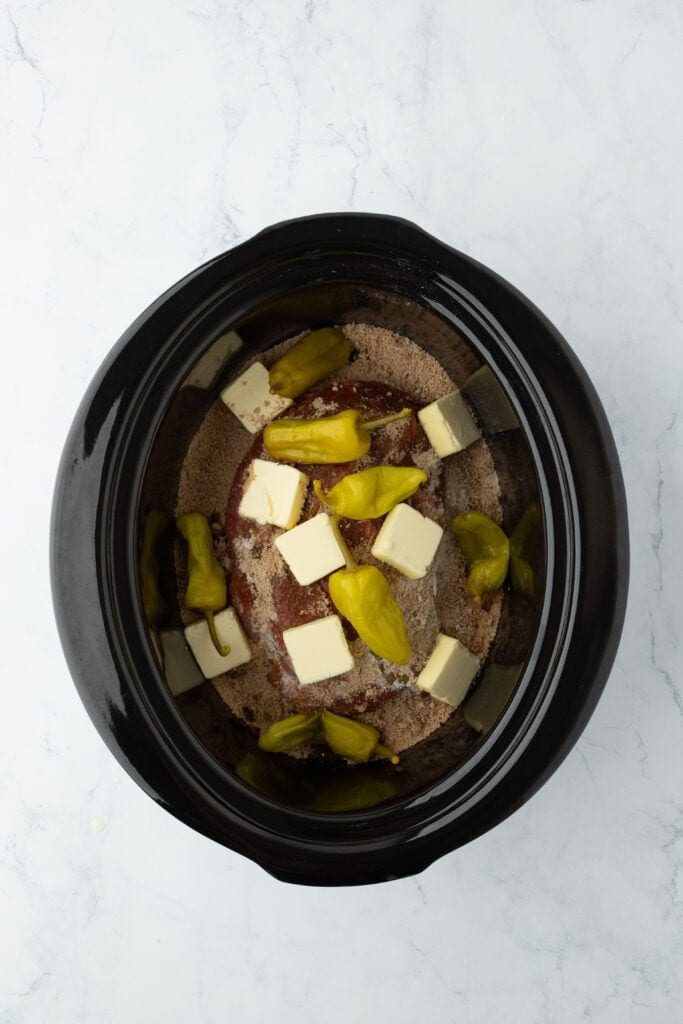 Butter and peppers added to a slow cooker