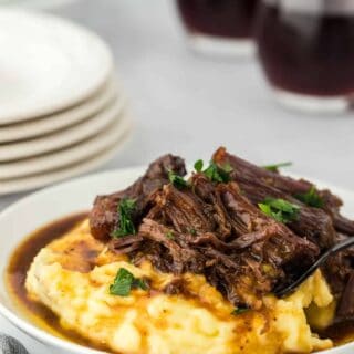 A large plate of a slow cooker Mississippi pot roast ready to serve over mashed potatoes