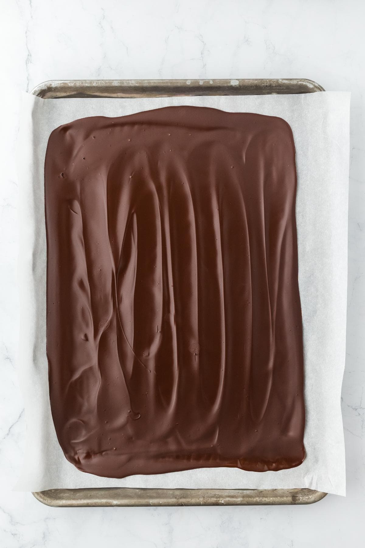 Melted dark chocolate spread in an even layer on a parchment-lined baking sheet