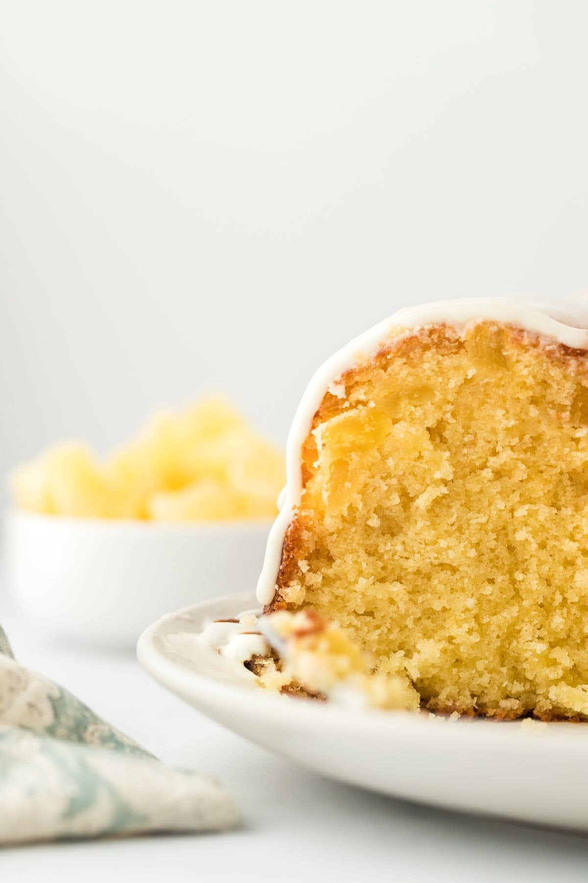 Close up of a slice of pineapple pound cake, showing its moist and fluffy texture, with a bowl of pineapple chunks in the background