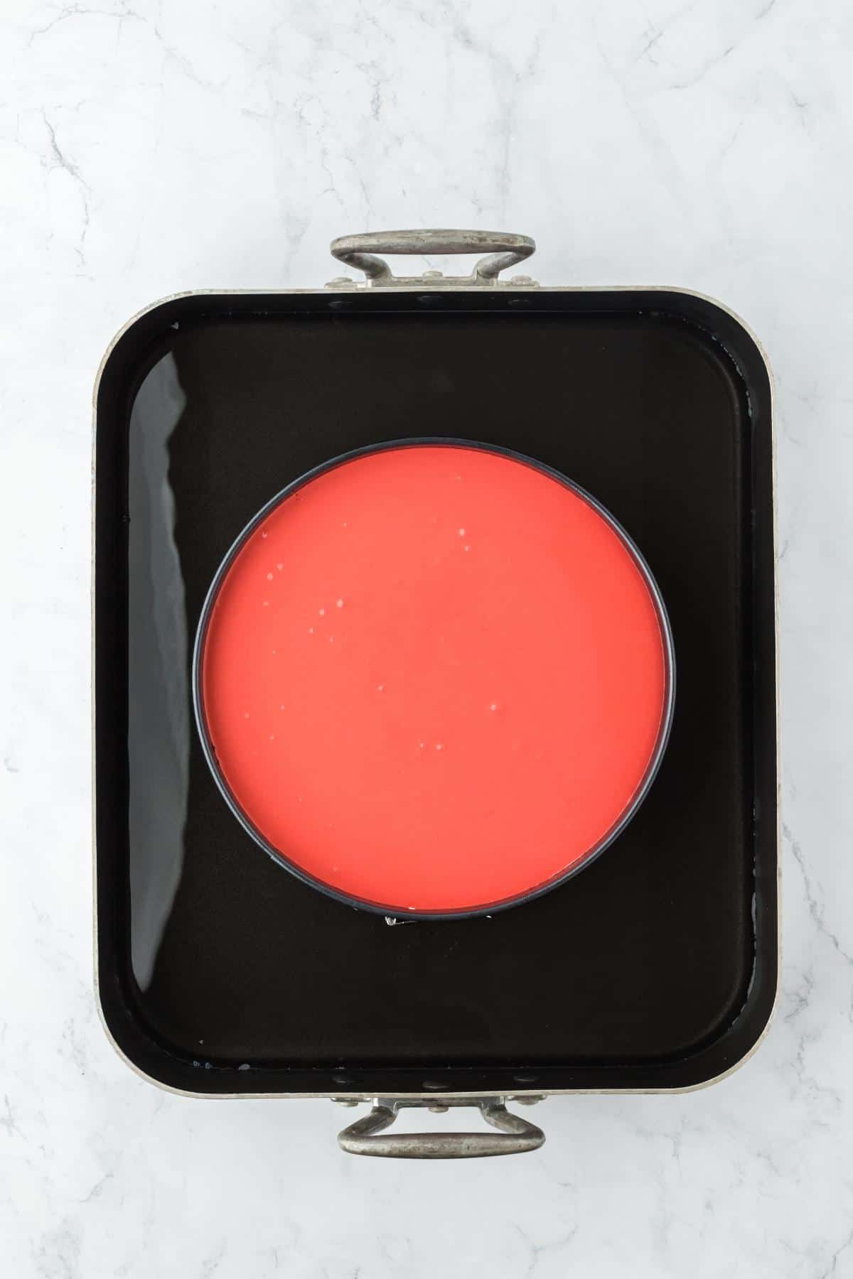 A red velvet cheesecake batter in a springform pan set inside a water bath, ready to bake