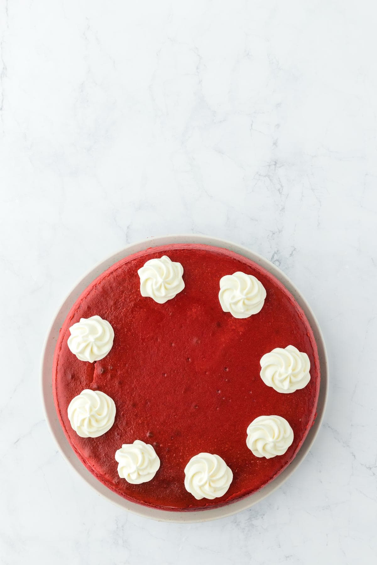 Finished red velvet cheesecake topped with evenly spaced swirls of cream cheese frosting