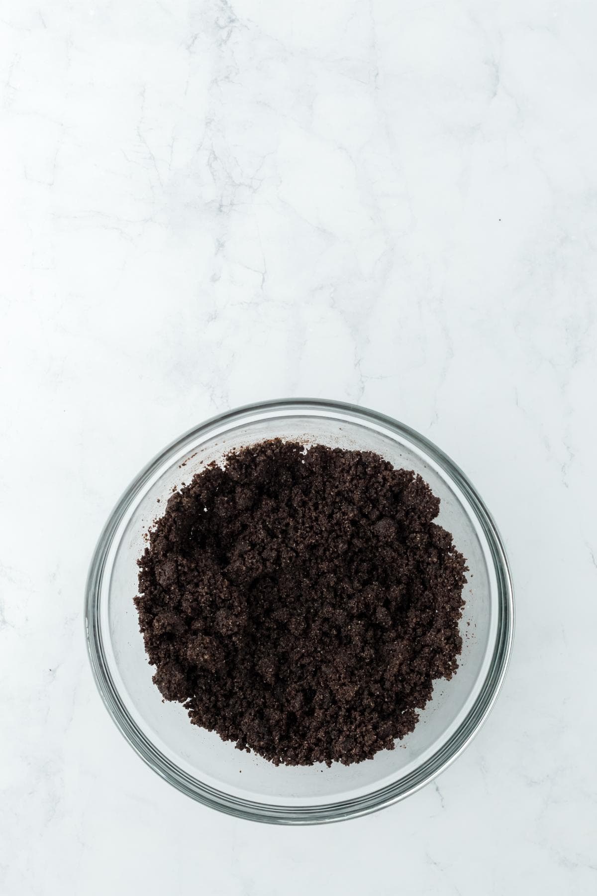 A glass bowl filled with crushed chocolate cookie crumbs for making cheesecake crust